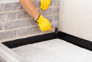 Man in Yellow Gloves Performing Waterproofing on Basement Wall